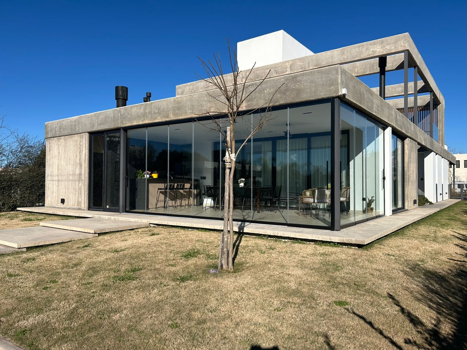 Fachada moderna con hormigón expuesto y amplios ventanales — proyecto CHACRAS DE LA VILLA, por GARCIA RECTA DESIGN, en X5105 Villa Allende